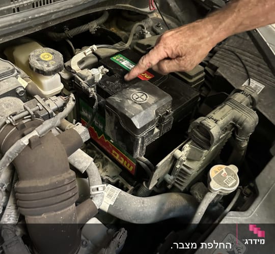 יד מצביעה על מצבר ברכב עם כבלים מחוברים